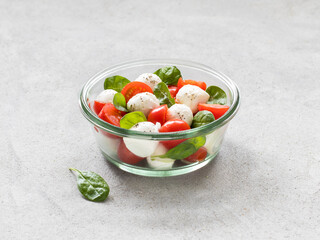 Italian food, Caprese salad of tomatoes, onions, spinach and mozzarella in a glass bowl on a light gray background