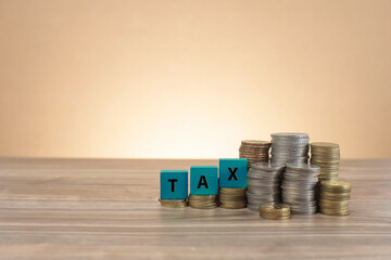 Message on TAX written on the wooden blocks on the stacked coins.  Business and tax concept