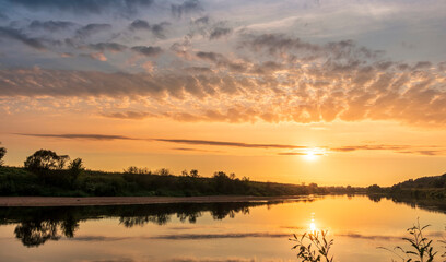 Fototapeta na wymiar Scenic view at beautiful summer river sunset with reflection on water with green bushes, calm water ,deep colorful cloudy sky and glow on horizon on a background, spring evening landscape