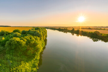 Scenic view at beautiful summer river sunset with reflection on water with green bushes, grass, golden sun rays, calm water ,deep cloudy sky and glow on a background, spring , evening landscape