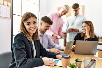 Group of young business workers working at the office. Hispanic woman smiling happy looking at the camera.