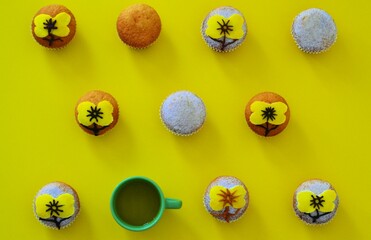 Rows of muffins decorated with powdered sugar and yellow flower shaped icing on a yellow background