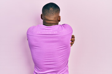 Young black man wearing casual pink sweater hugging oneself happy and positive from backwards. self...