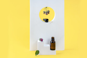 a bottle of burdock oil, burdock flowers and geometric podiums on a yellow background