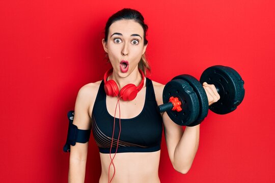 Young hispanic girl wearing sportswear using dumbbells scared and amazed with open mouth for surprise, disbelief face