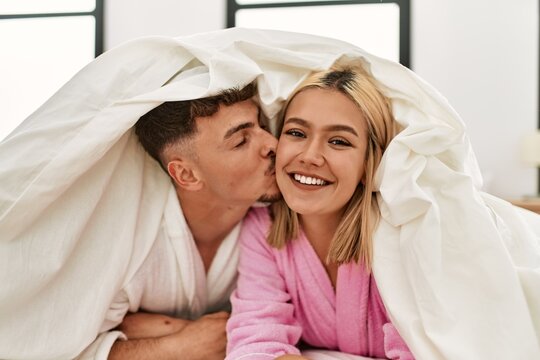Young caucasian couple covering with bedsheet and smiling happy lying on the bed at home.