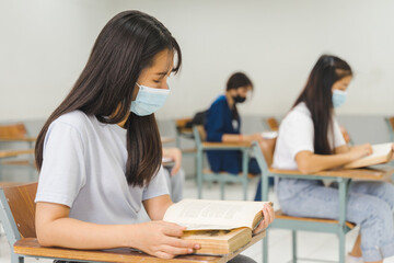 Obraz premium Asian college students back to school wear protective facemask and keep social distance studying in the classroom