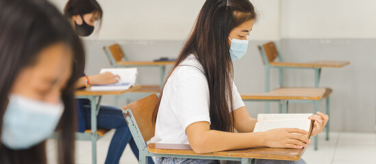 Asian college students back to school wear protective facemask and keep social distance studying in the classroom