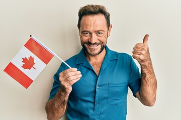 Middle age man holding canada flag smiling happy and positive, thumb up doing excellent and approval sign