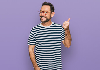 Middle age man wearing casual clothes and glasses smiling with happy face looking and pointing to the side with thumb up.