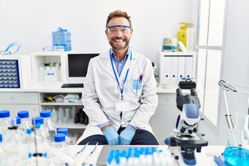 Middle age man working at scientist laboratory looking positive and happy standing and smiling with...
