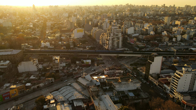 Cinematic aerial shot showing golden city of Buenos Aires during epic sunset. Panorama view of buildings and passing train.