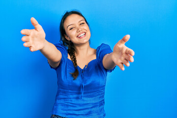 Young hispanic girl wearing casual clothes looking at the camera smiling with open arms for hug. cheerful expression embracing happiness.