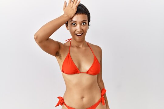 Young hispanic woman with short hair wearing bikini surprised with hand on head for mistake, remember error. forgot, bad memory concept.