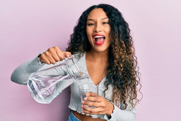 Young latin woman pouring water smiling and laughing hard out loud because funny crazy joke.