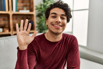 Young hispanic man smiling happy saying hello with hand at home.