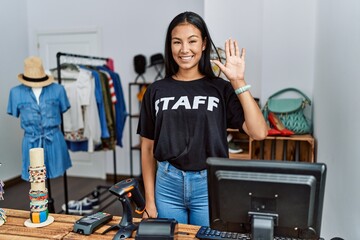 Young hispanic woman working as staff at retail boutique waiving saying hello happy and smiling, friendly welcome gesture