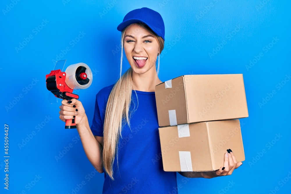 Canvas Prints young caucasian woman holding packages and packing tape sticking tongue out happy with funny express