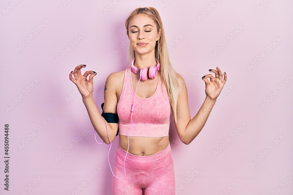 Poster young beautiful caucasian woman wearing gym clothes and using headphones relax and smiling with eyes