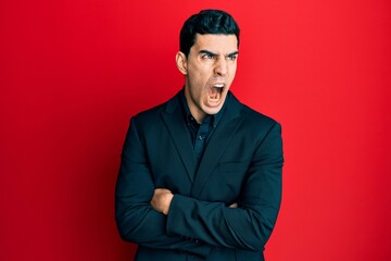 Obraz premium Handsome hispanic business man with arms crossed gesture angry and mad screaming frustrated and furious, shouting with anger. rage and aggressive concept.