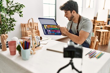Obraz na płótnie Canvas Young hispanic artist man smiling happy making online paint class at art studio.