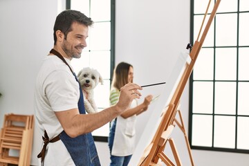 Two hispanic students smiling happy and holding dog painting at art studio.