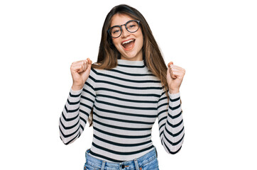 Young beautiful teen girl wearing casual clothes and glasses celebrating surprised and amazed for success with arms raised and open eyes. winner concept.