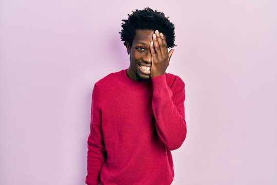 Young african american man wearing casual clothes covering one eye with hand, confident smile on face and surprise emotion.