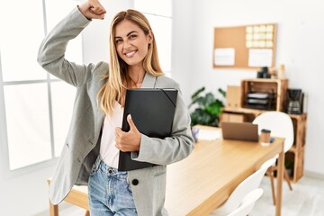 Blonde business woman at the office strong person showing arm muscle, confident and proud of power