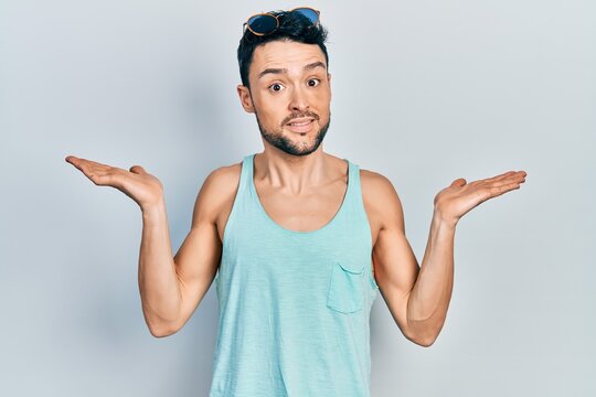 Young hispanic man wearing summer style clueless and confused with open arms, no idea and doubtful face.
