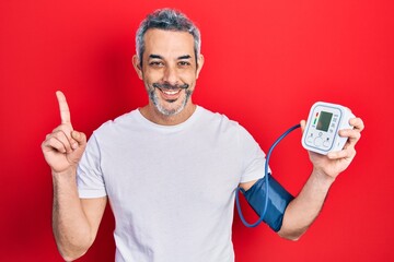 Handsome middle age man with grey hair using blood pressure monitor surprised with an idea or...