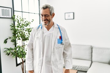 Middle age hispanic man wearing doctor uniform and stethoscope at waiting room winking looking at...