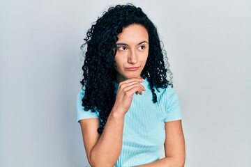 Fototapeta na wymiar Young hispanic woman with curly hair wearing casual blue t shirt with hand on chin thinking about question, pensive expression. smiling with thoughtful face. doubt concept.