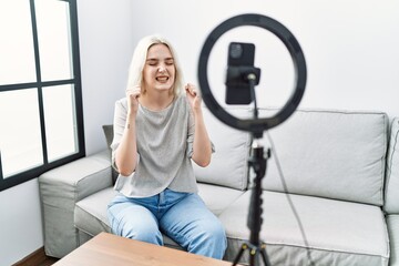 Fototapeta na wymiar Young caucasian woman recording vlog tutorial with smartphone at home excited for success with arms raised and eyes closed celebrating victory smiling. winner concept.