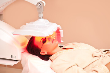 Woman lying on a table with protect glasses on eyes have a skin treatment under beauty device....