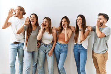Group of young friends standing together over isolated background shouting and screaming loud to side with hand on mouth. communication concept.