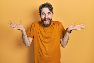 Caucasian man with beard wearing casual yellow t shirt celebrating crazy and amazed for success with arms raised and open eyes screaming excited. winner concept