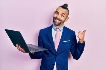 Young hispanic man working using computer laptop pointing thumb up to the side smiling happy with open mouth