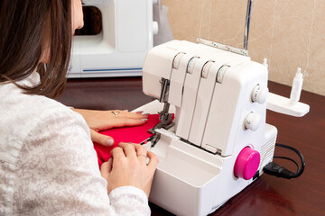A woman is scribbling fabric on a white sewing machine holding it with her hands. The process of...
