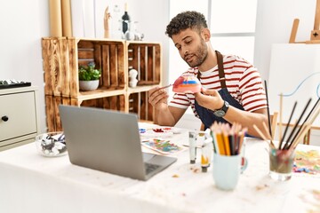 Young arab artist man using laptop drawing ceramic at art studio.