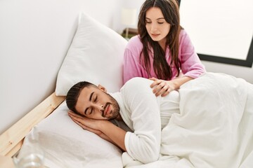 Fototapeta premium Young hispanic woman looking her sleepy boyfriend at bed.