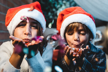 Little girl and boy having with confetti during Christmas time outdoor at home patio - Brother and...
