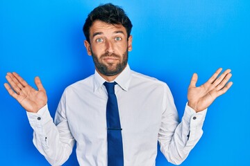 Handsome man with beard wearing business shirt and tie clueless and confused with open arms, no idea and doubtful face.