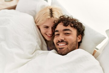 Young beautiful couple lying in bed and covering with blanket at home.