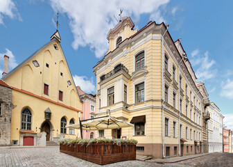 Fototapeta na wymiar Medieval Tallinn, panoramic image of old town. Ancient houses on cobbled street in medieval center. Wooden terrasse of outdoor cafe or restaurant. Daylight, blue sky with cumulous clouds.