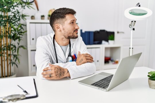 Young doctor working at the clinic using computer laptop smiling looking to the side and staring away thinking.