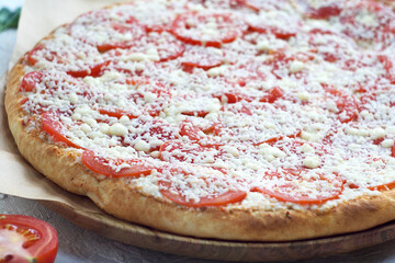 Pizza margarita with tomatoes and cheese on a wooden board.