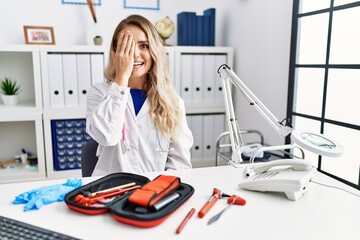 Young beautiful doctor woman with reflex hammer and medical instruments covering one eye with hand,...