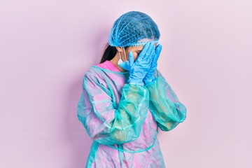 Young brunette woman wearing surgeon uniform and medical mask with sad expression covering face with hands while crying. depression concept.