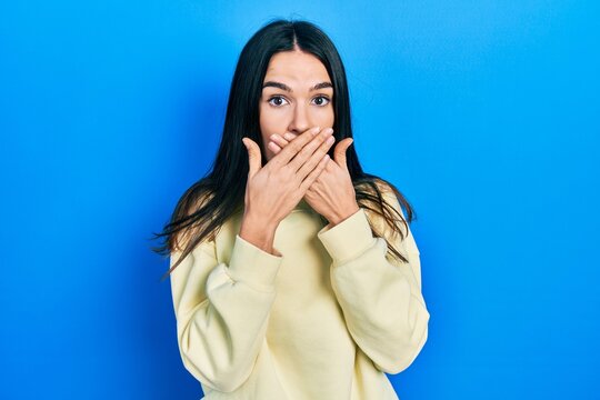 Young brunette woman wearing casual sweatshirt shocked covering mouth with hands for mistake. secret concept.
